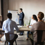 Man writing on white board while leading a corporate training session.