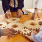 Team collaborating to connect wooden gears, symbolizing conflict and innovation working together.