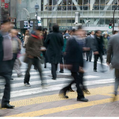 Blurry image of busy professionals crossing a crowded city street, representing the fast-paced nature of modern work and the pressure to always be moving.