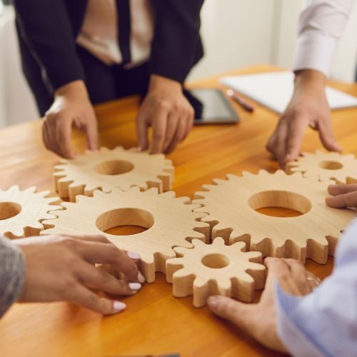 Team collaborating to connect wooden gears, symbolizing conflict and innovation working together.